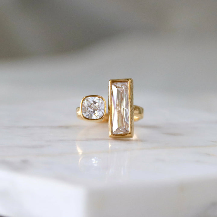Open front gold ring with two different cut diamonds on a marble surface