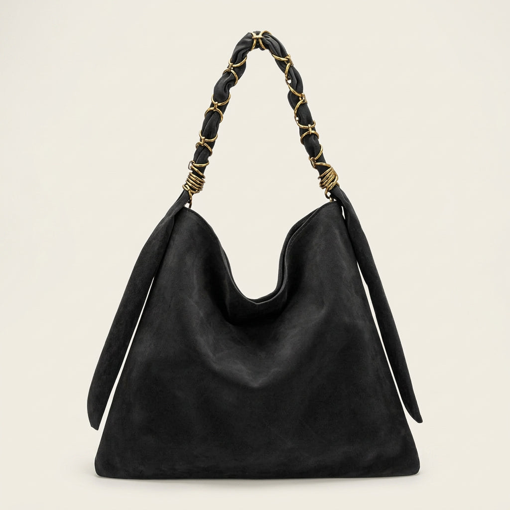 A black vegan suede slouchy shoulder bag with a braided black leather strap accented by gold-tone metal rings, shown against a plain white background.