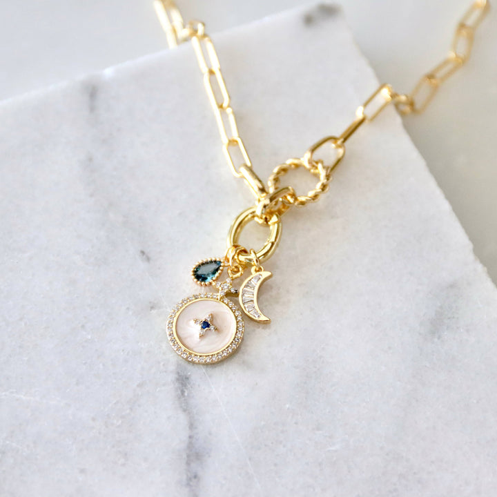 Gold chain necklace with gemstone charms on a marble surface