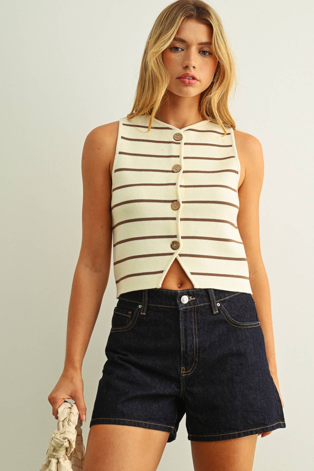 Woman wearing a striped sleeveless top and denim shorts against a plain background