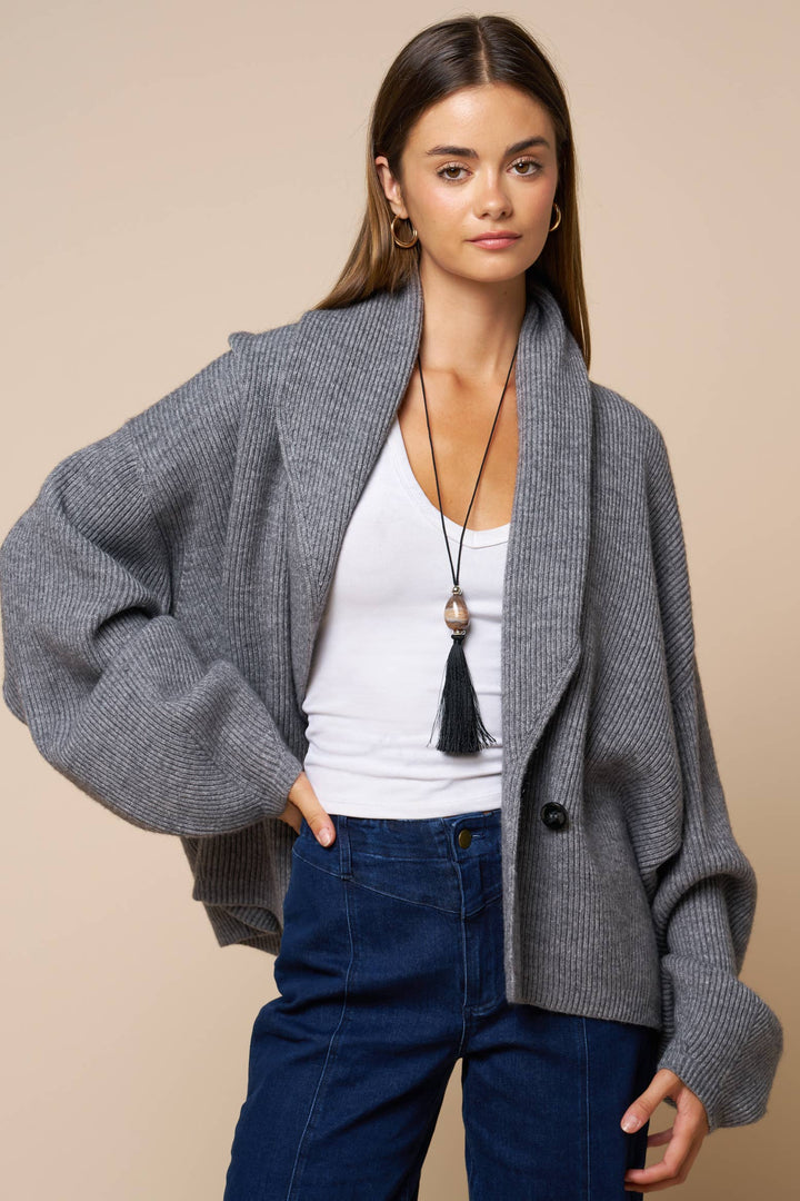 Woman wearing a gray cardigan over a white top and blue jeans on a beige background