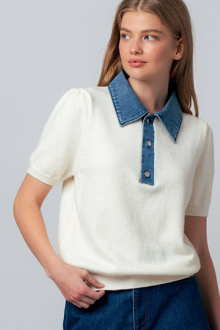 Woman wearing a white sweater with a blue collar against a gray background