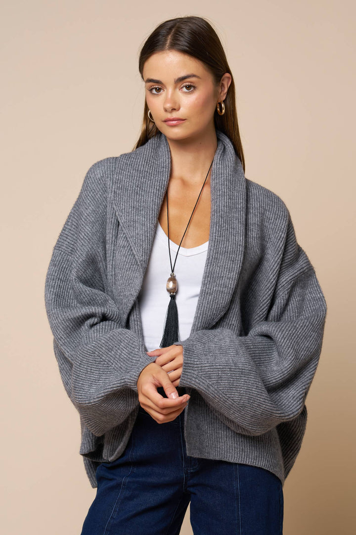 Woman wearing a gray cardigan over a white top and blue jeans on a beige background