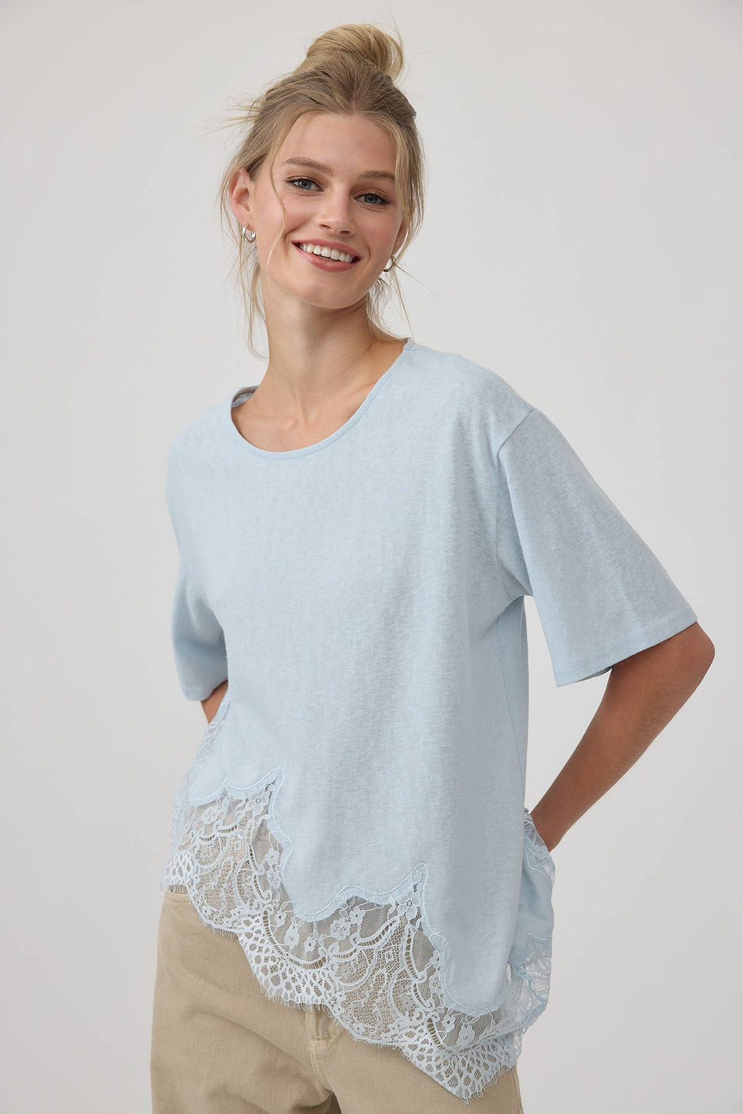 Woman wearing a light blue top with lace trim on a plain background