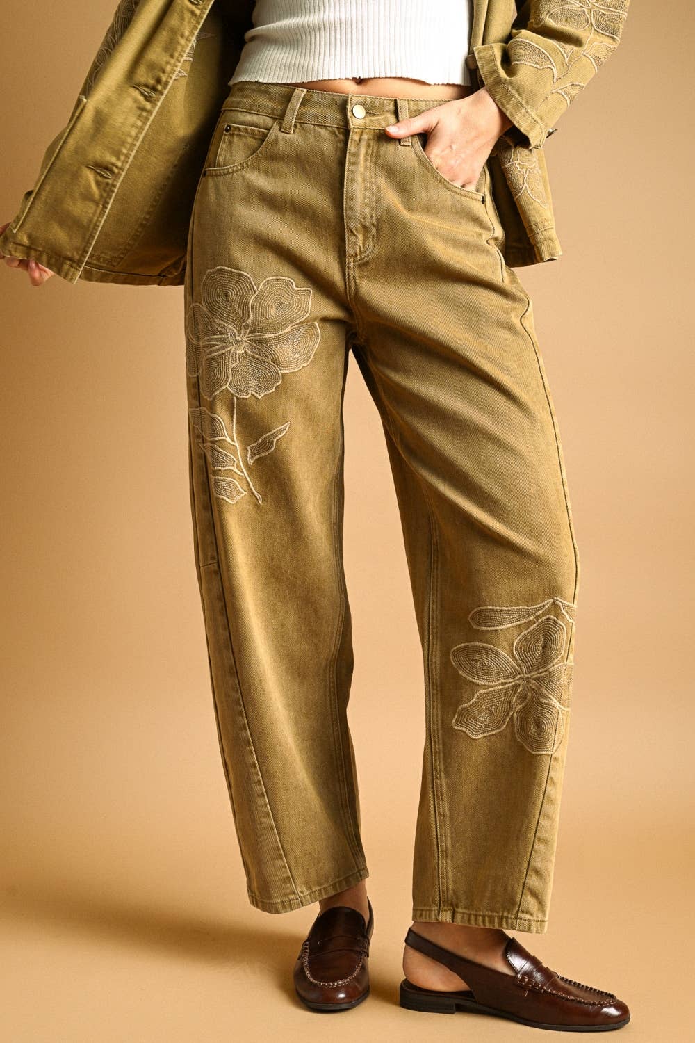 Woman wearing brown floral embroidered pants on a beige background