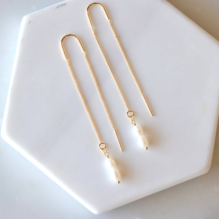 Gold and pearl dangling earrings on a white hexagonal dish