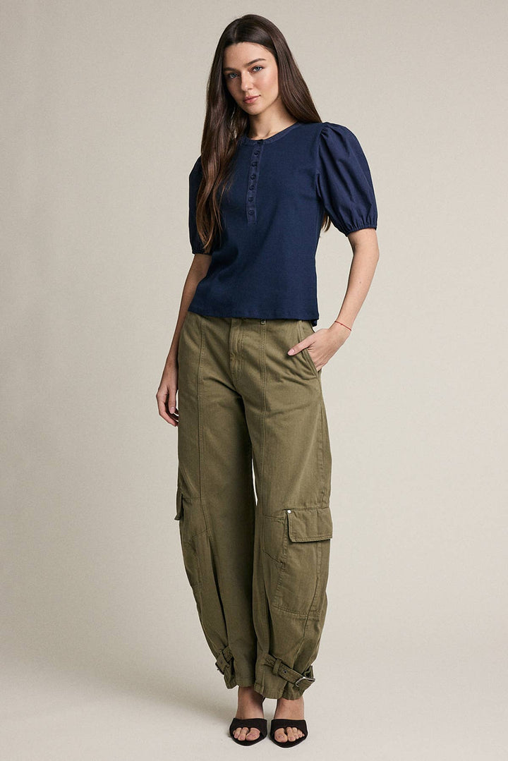A woman modeling a navy blue short-sleeve top with puff sleeves and olive green cargo pants, standing against a plain beige studio background.