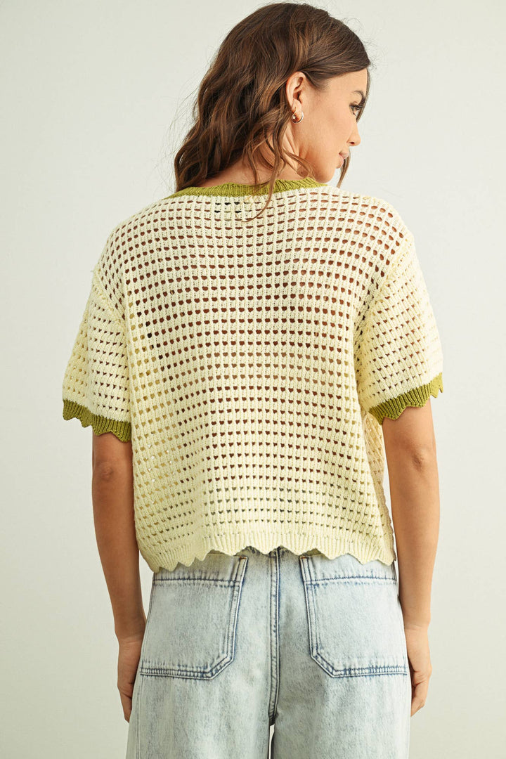 Woman wearing an off-white crochet top with green trim on a plain background