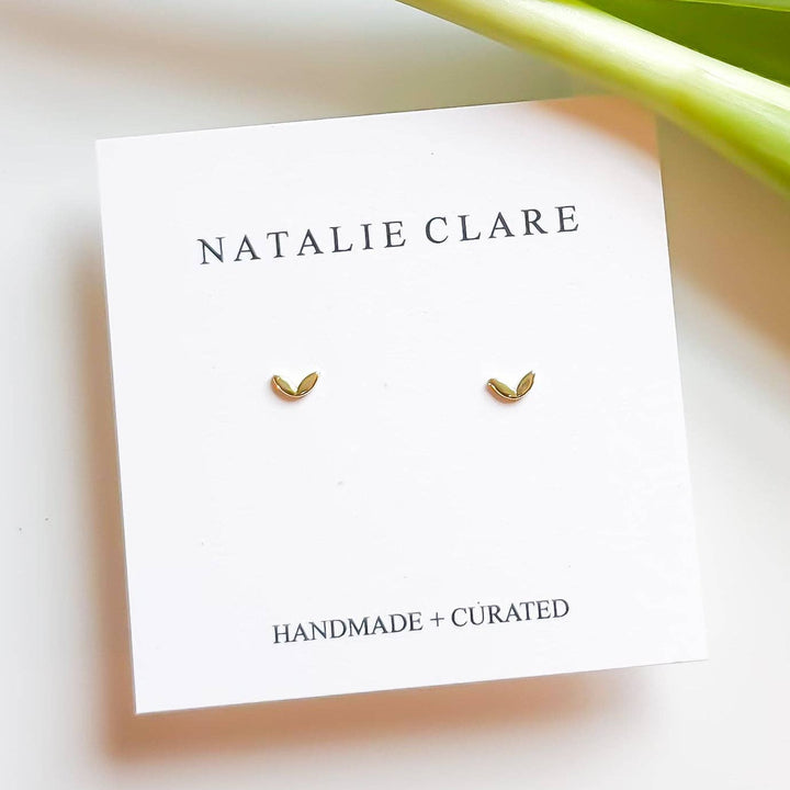 Gold tiny stud earrings on a 'Natalie Clare' branded card with a blurred background