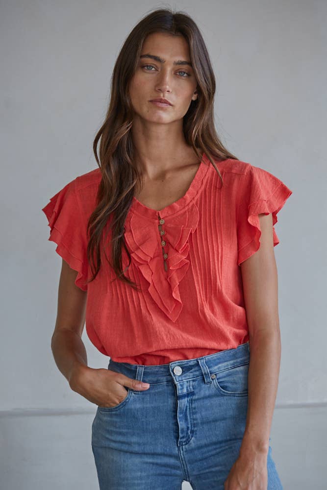 Woman wearing a red blouse with ruffled details and blue jeans against a plain background