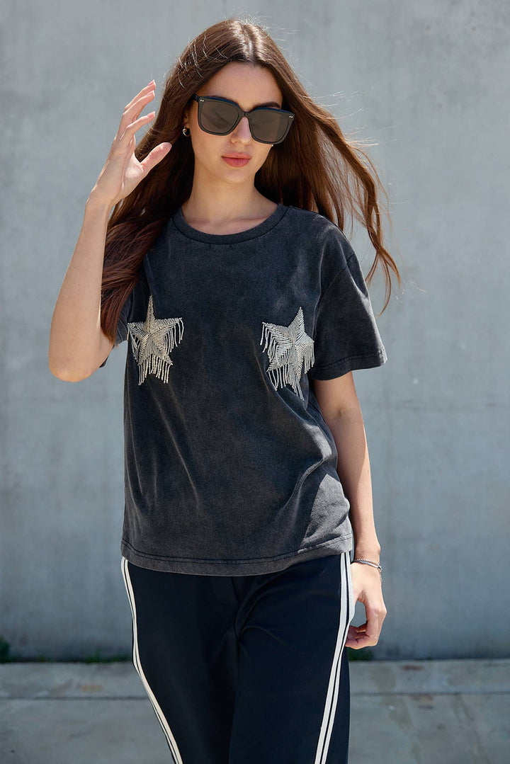 Woman wearing a dark t-shirt with star  fringe design against a gray wall.