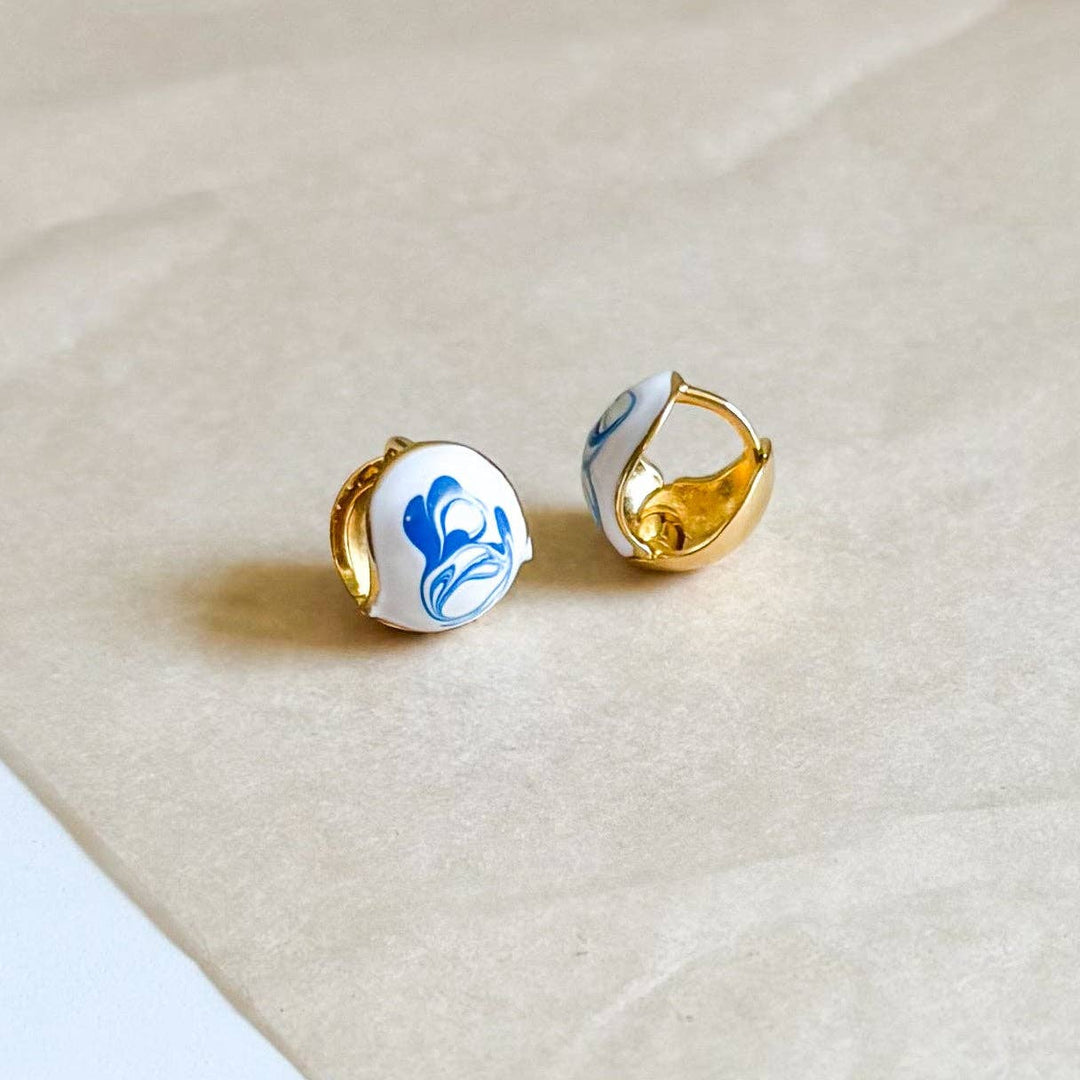 Pair of gold earrings with blue and white designs on a beige surface