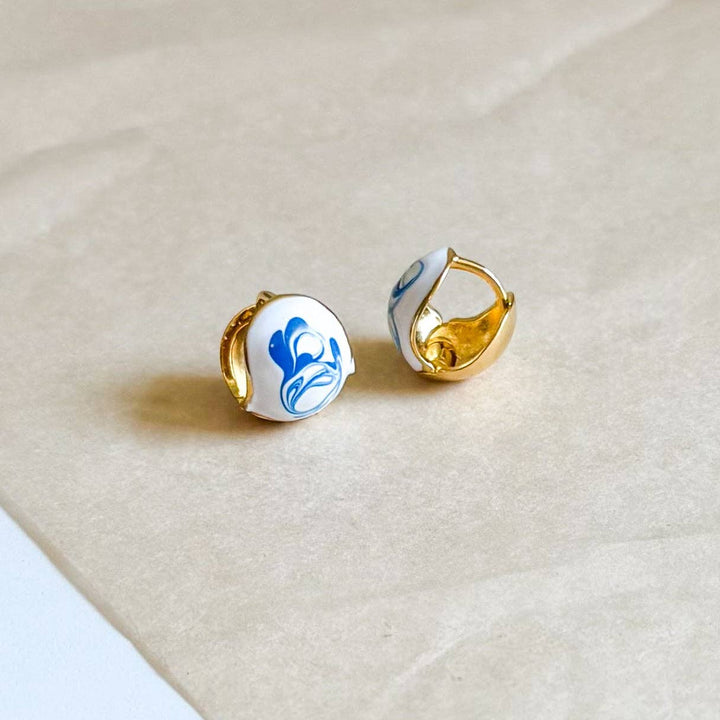 Pair of gold earrings with blue and white designs on a beige surface