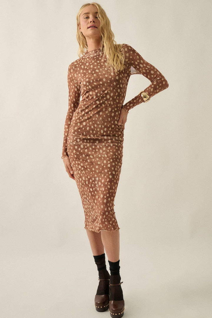 A woman modeling a long-sleeve, high-neck midi dress with an allover brown and beige animal print, paired with black socks and brown platform shoes, against a plain light beige studio background.