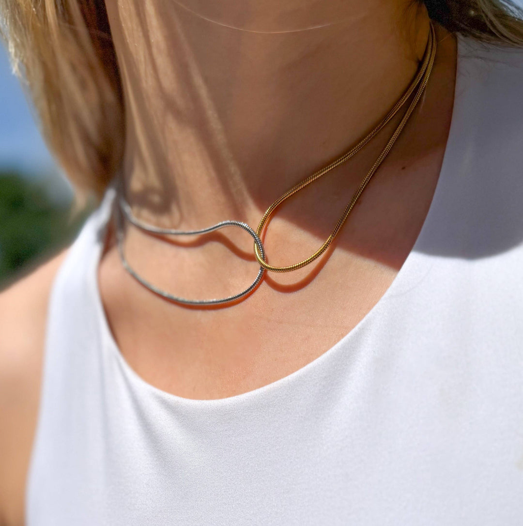 Close-up of a woman wearing a gold and silver necklace with a blurred natural background
