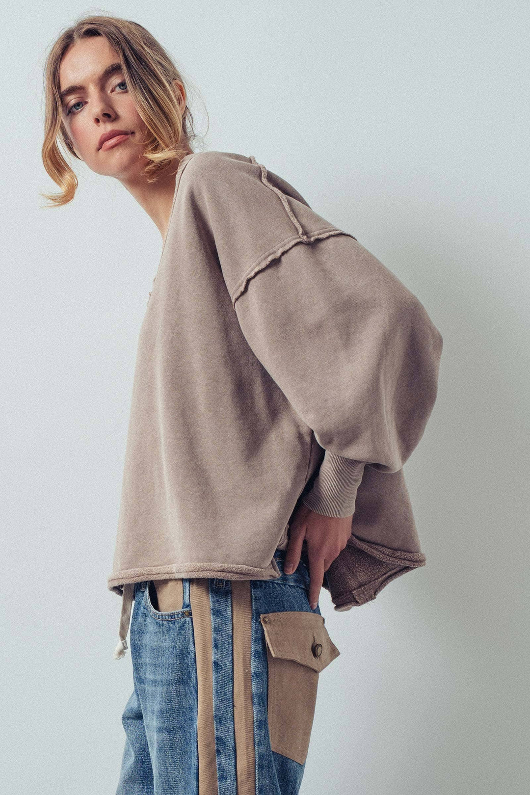 Person wearing a beige oversized sweatshirt and blue jeans with a white background