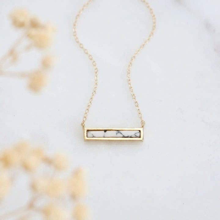 Dainty gold necklace with white turquoise inlay on a light background