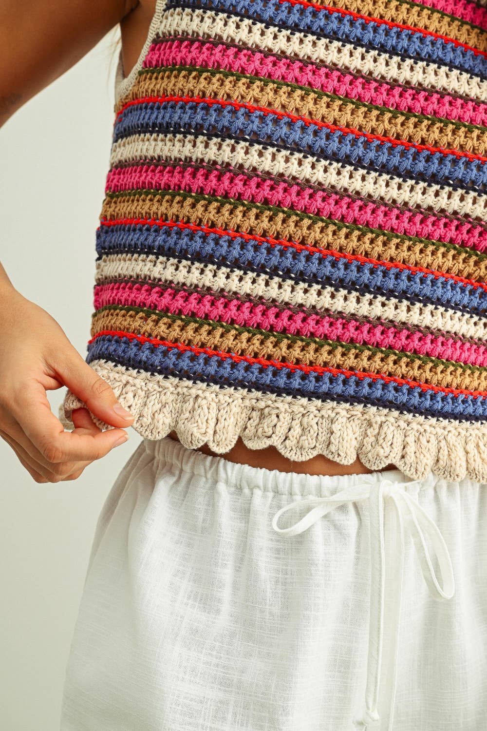 Colorful striped sleeveless crochet knit top with lace trim worn by a person, on a plain background.
