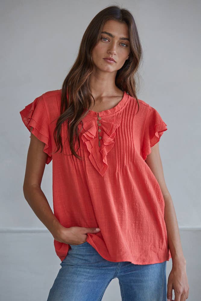 Woman wearing a red blouse with ruffled sleeves and blue jeans against a plain background
