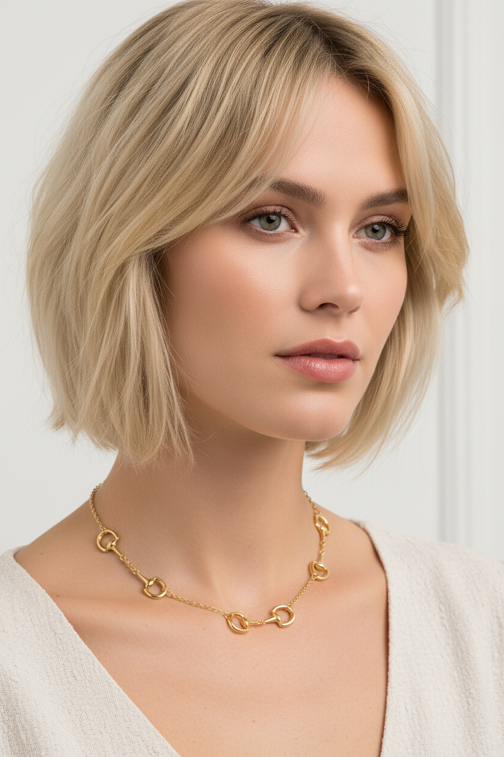 A gold horsebit chain necklace featuring five horsebit links spaced evenly along a delicate cable chain, with a lobster clasp closure at the top, shown on a plain white background.