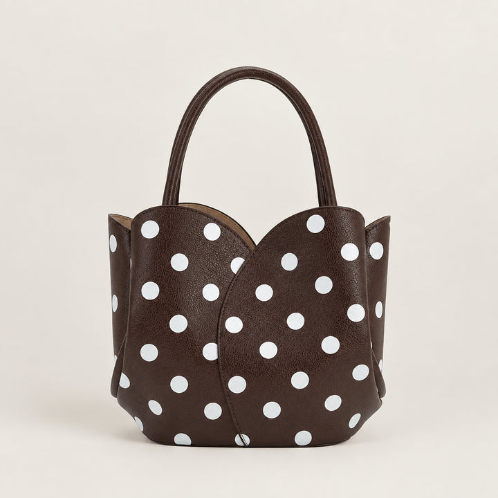 A dark brown textured leather handbag with a white polka dot pattern, featuring a single top handle and a structured, scalloped front design, shown against a plain white background.