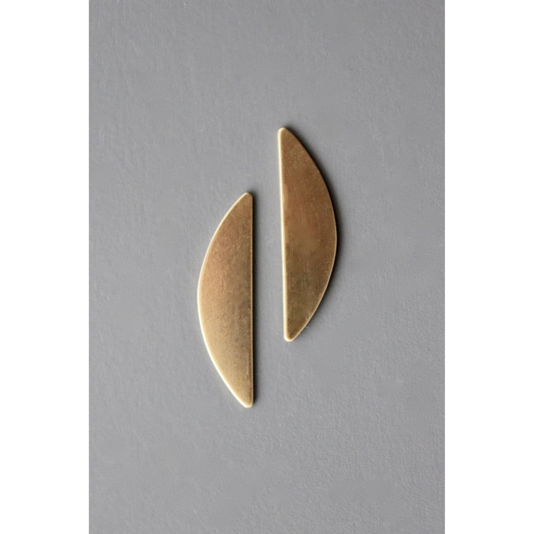 Two gold leaf-shaped earrings on a gray background