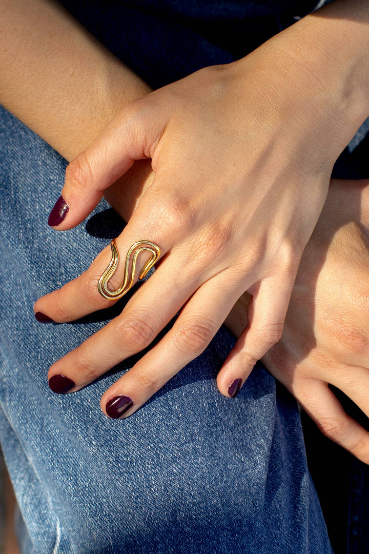 Close-up of a hand wearing a gold ring with a snake design, against a denim background.