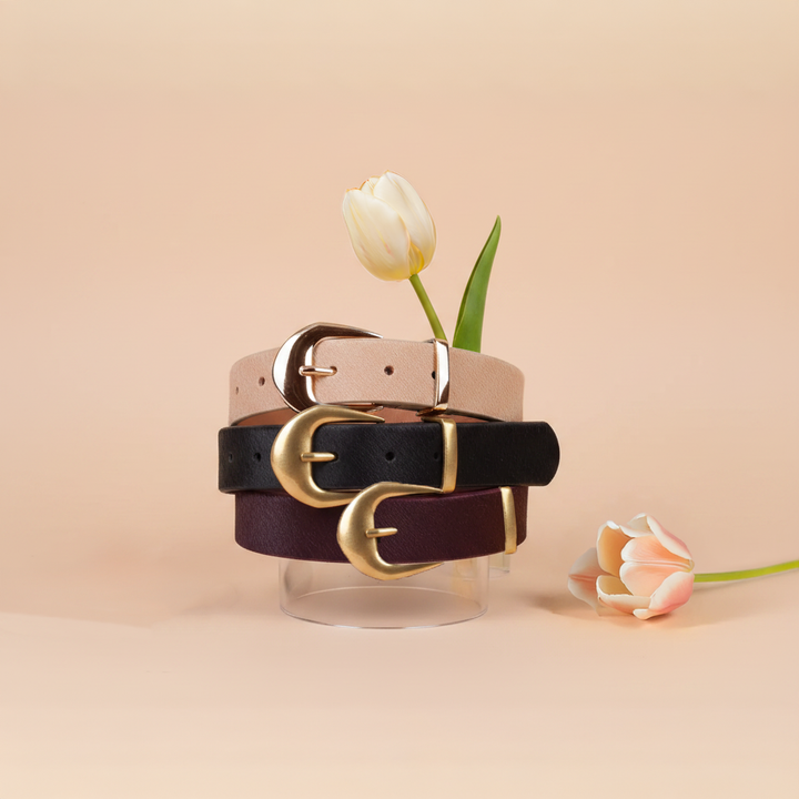 Three calf hair leather belts with gold buckles on a beige background with flowers.