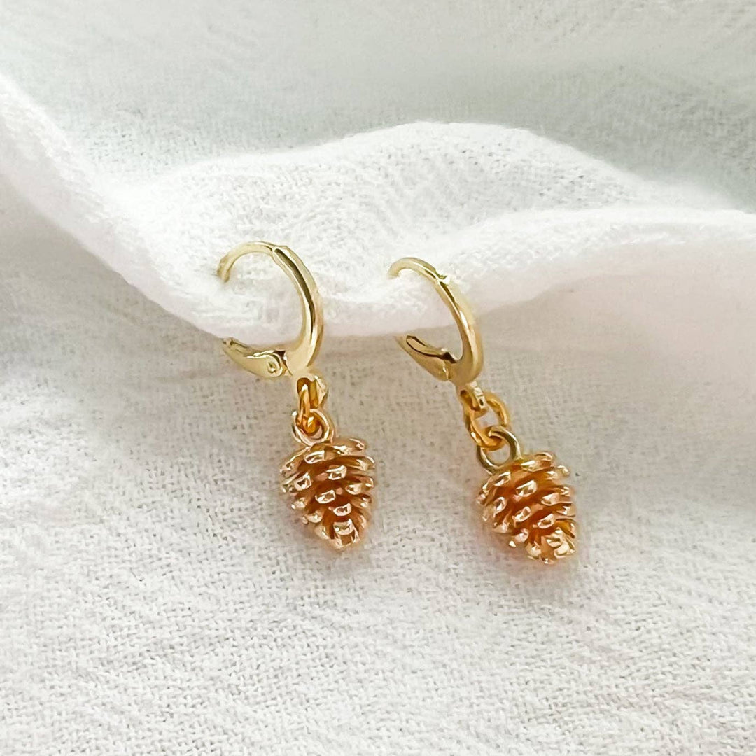 Gold pinecone earrings on a white fabric background