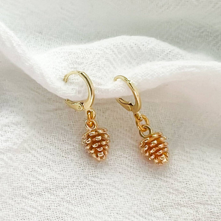 Gold pinecone earrings on a white fabric background
