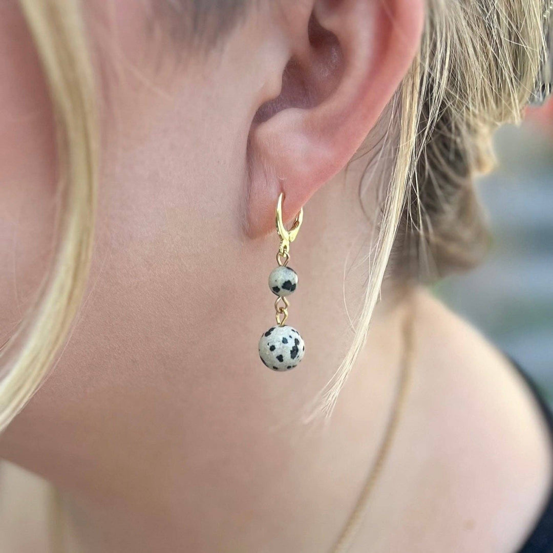 A close-up of a person's ear wearing a gold hoop earring with two dangling beads with white and black speckles
