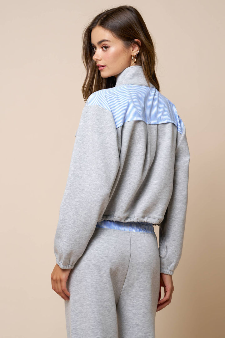 Woman wearing a gray and light blue sweatshirt jacket on a beige background