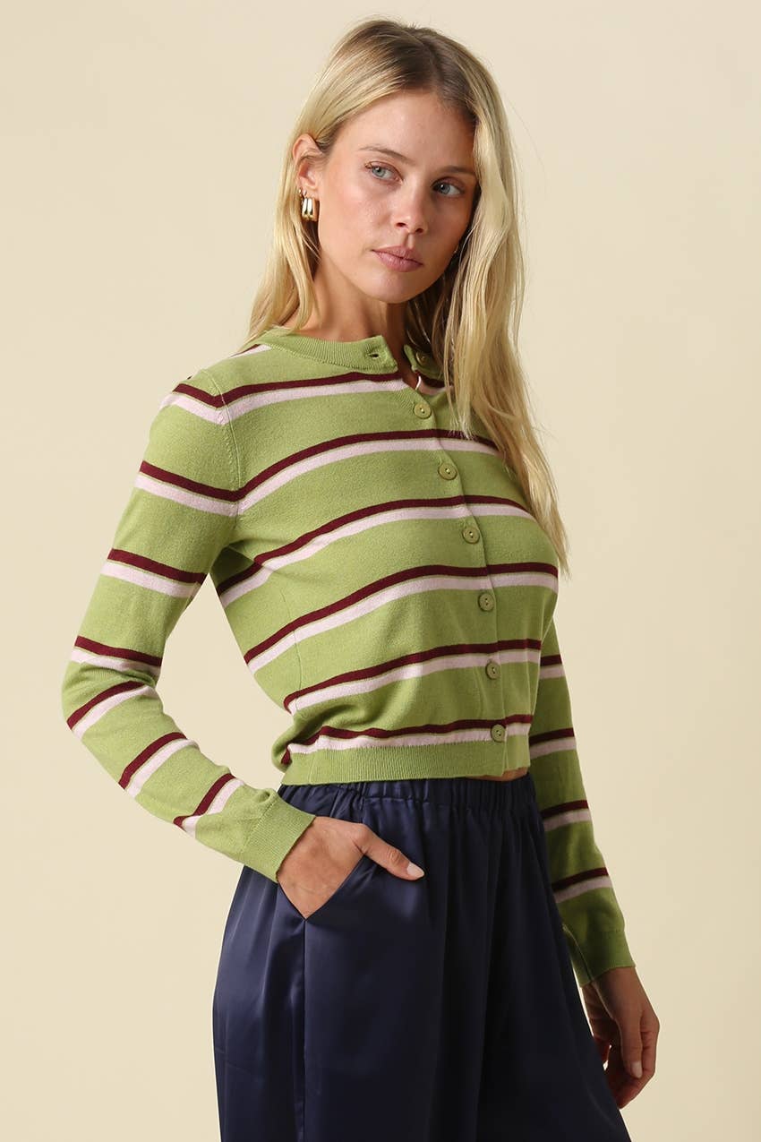 A woman modeling a green striped long-sleeve button-up cardigan with burgundy and cream stripes, paired with a navy skirt, against a solid beige background.