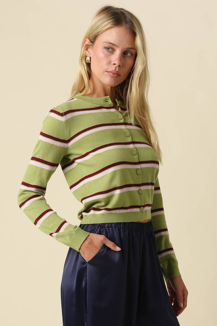 A woman modeling a green striped long-sleeve button-up cardigan with burgundy and cream stripes, paired with a navy skirt, against a solid beige background.