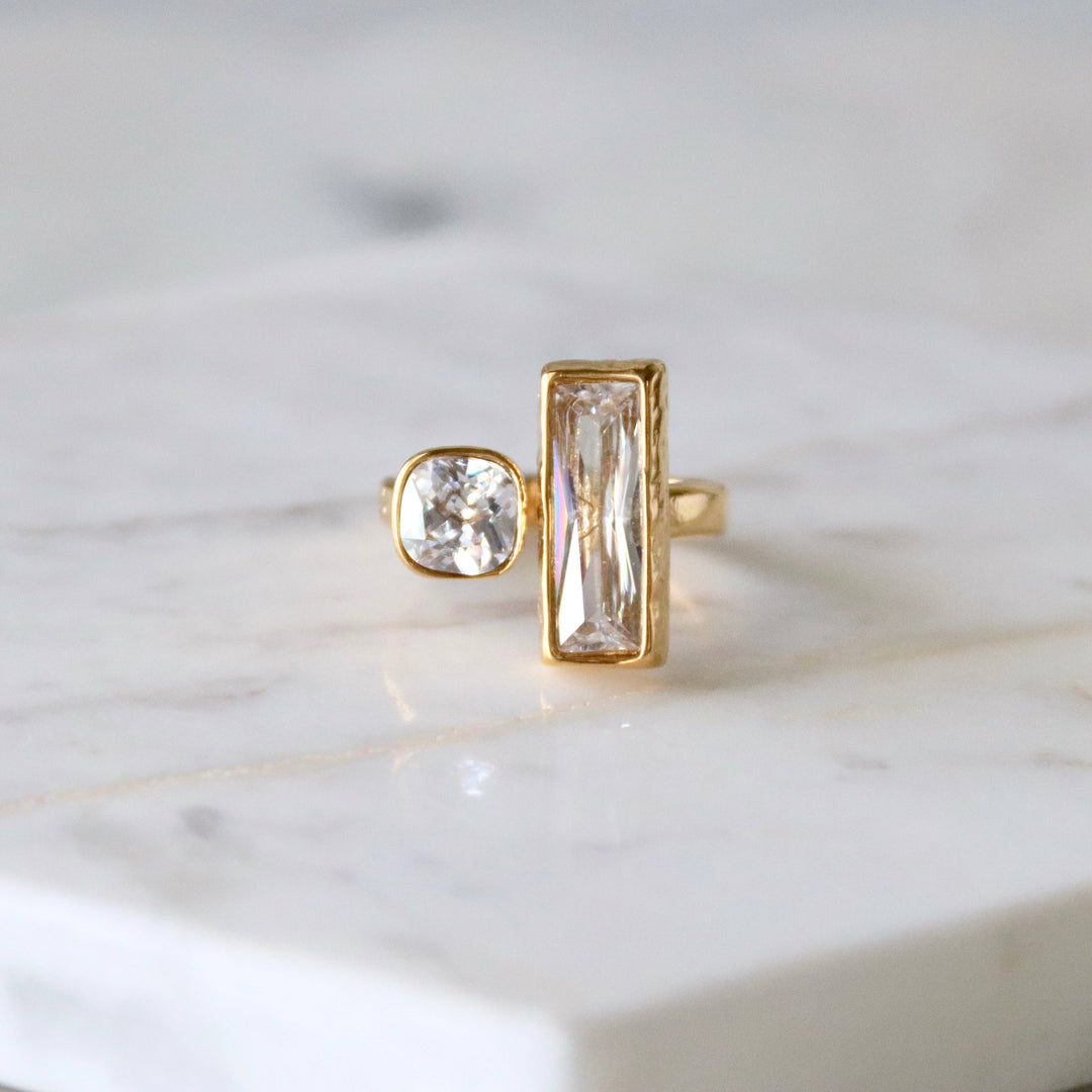 Gold ring with two different cut Cz gemstones on a marble surface