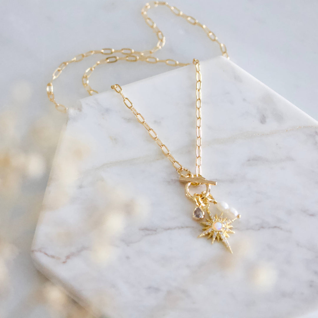 Gold necklace with a sun pendant on a marble surface