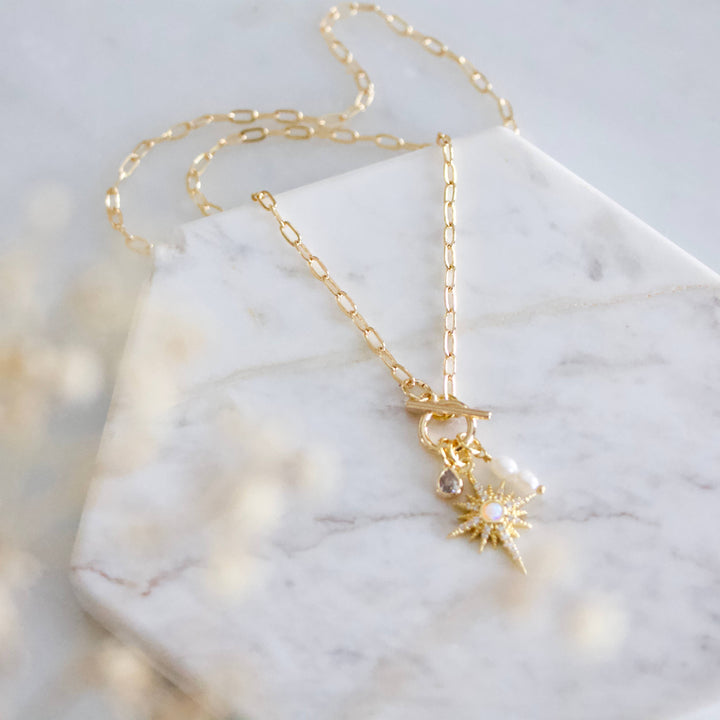 Gold necklace with a sun pendant on a marble surface