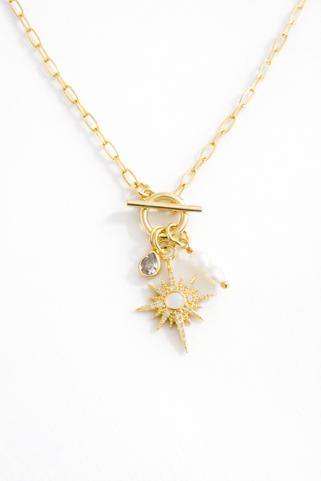 Gold necklace with star-shaped pendant  and pearl charm on a white background