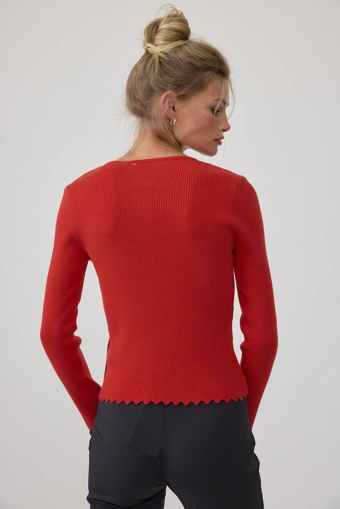 Woman wearing a red sweater with a scalloped hem on a plain background