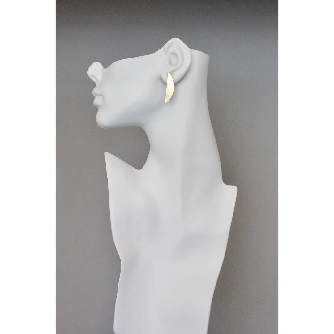 White mannequin head with a single gold leaf shaped earring on a gray background