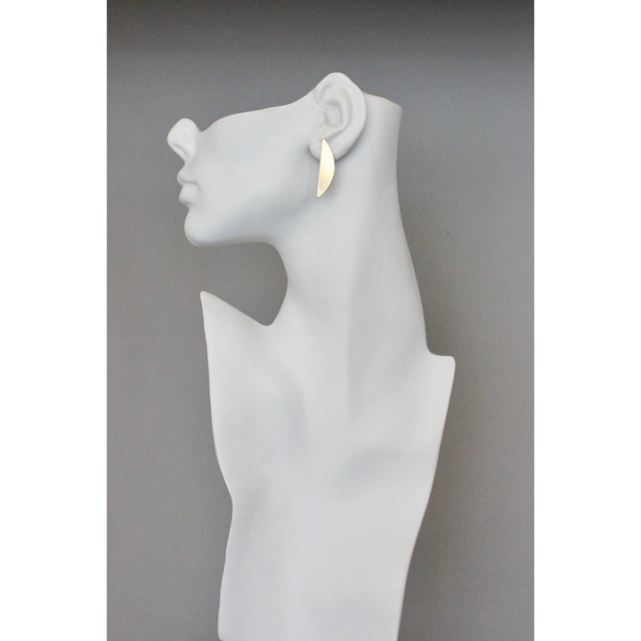 White mannequin head with a single gold leaf shaped earring on a gray background