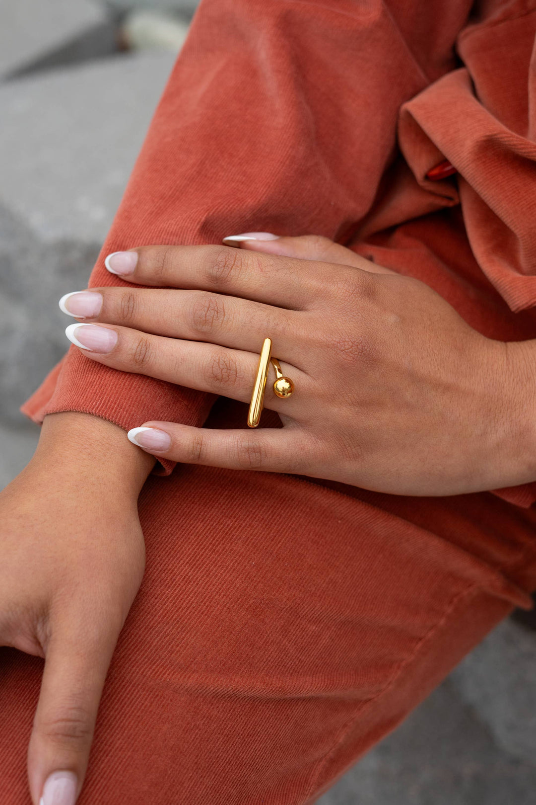 Close-up of a hand wearing a gold adjustable ring on a rust-colored fabric background