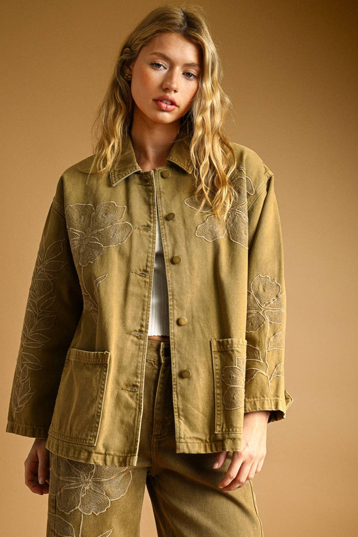 Woman wearing a light brown denim jacket with floral embroidery on a beige background
