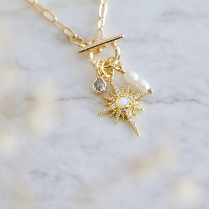 Gold necklace with star-shaped pendant and pearl on marble background
