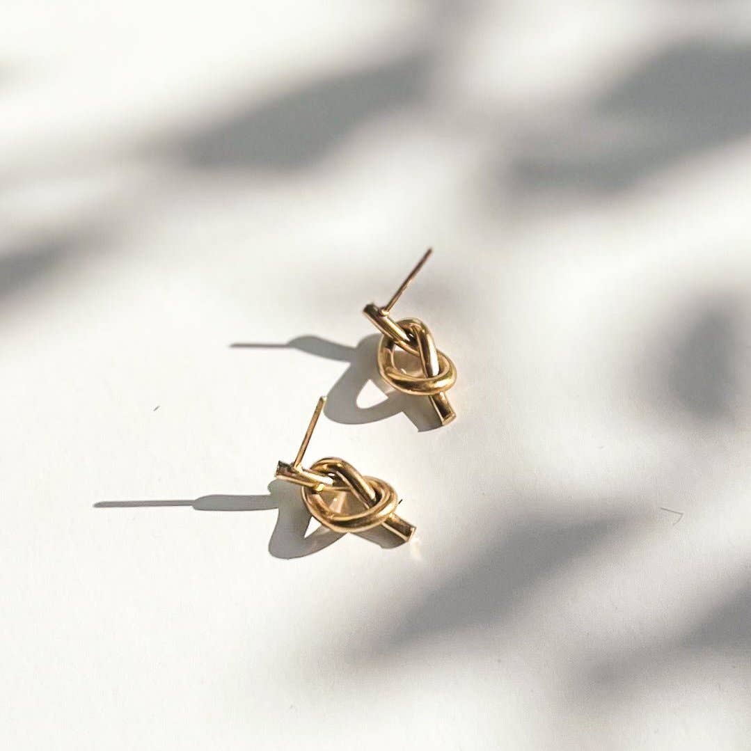 Pair of gold knot stud earrings on a light background