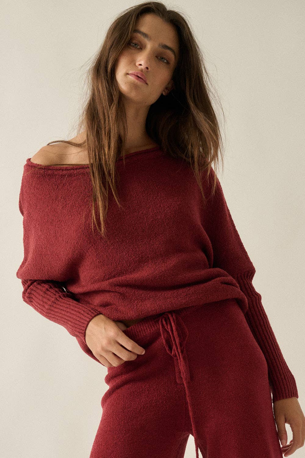 Woman wearing a red off-shoulder sweater and pants set against a plain background