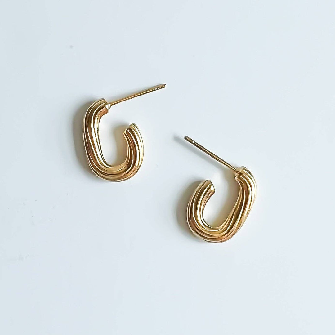 A pair of gold-toned, twisted hoop-style stud earrings on a clean, light off-white background.