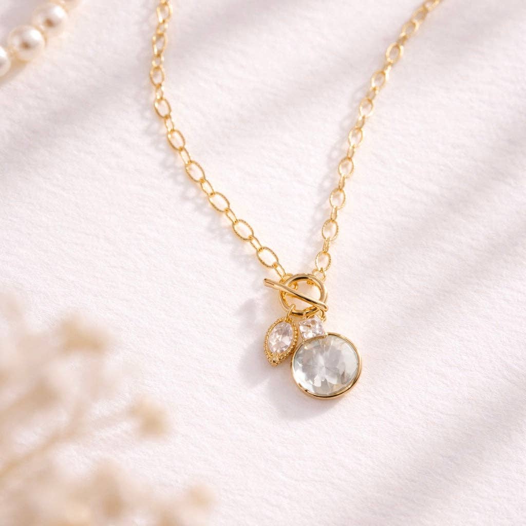 Gold charm necklace with a fresh water pearl pendant on a soft white background