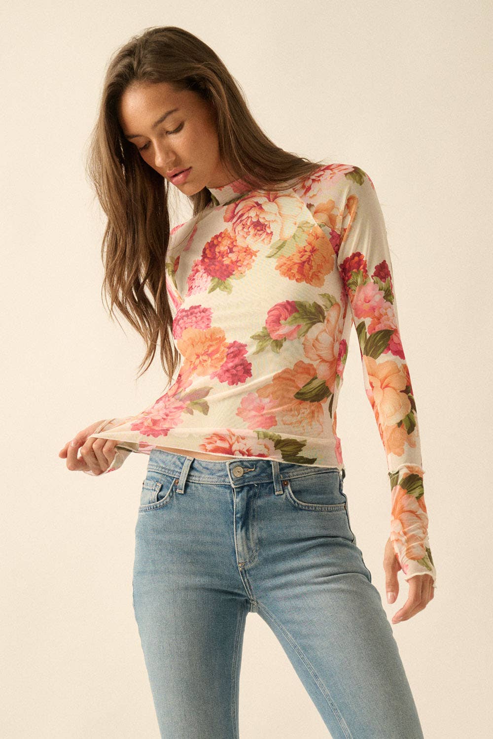 Woman wearing a floral mesh long-sleeve top and jeans on a plain background