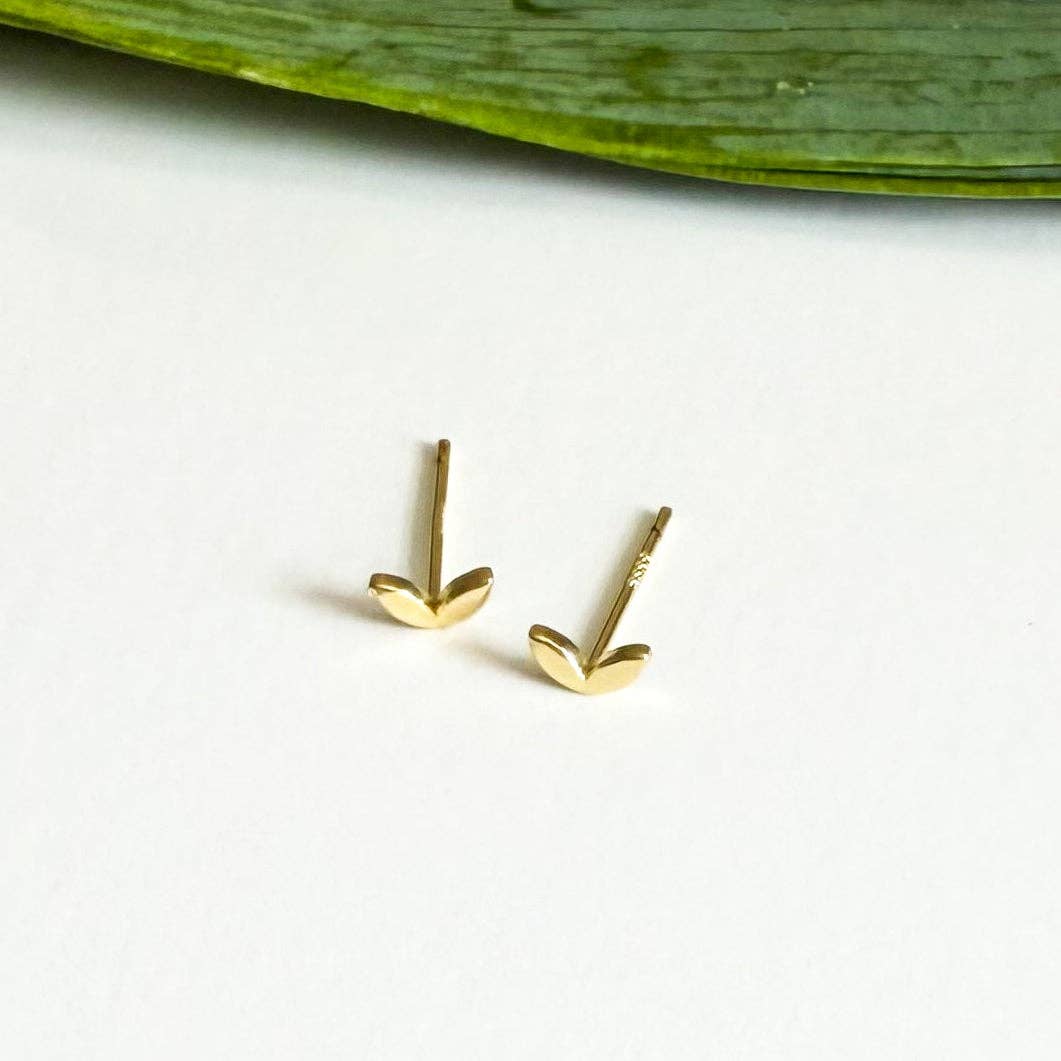 Gold heart-shaped earrings on a white background with a green leaf